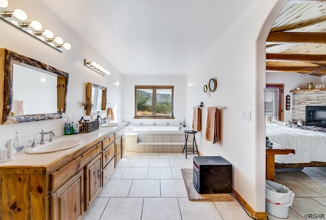 bathroom featuring vanity, tiled bath, a stone fireplace, tile patterned floors, and beamed ceiling