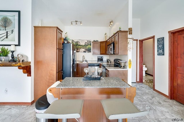 kitchen with appliances with stainless steel finishes, sink, a kitchen bar, light stone counters, and kitchen peninsula