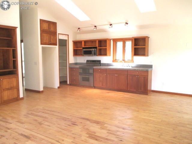 kitchen featuring sink, stainless steel counters, appliances with stainless steel finishes, vaulted ceiling with skylight, and light hardwood / wood-style floors