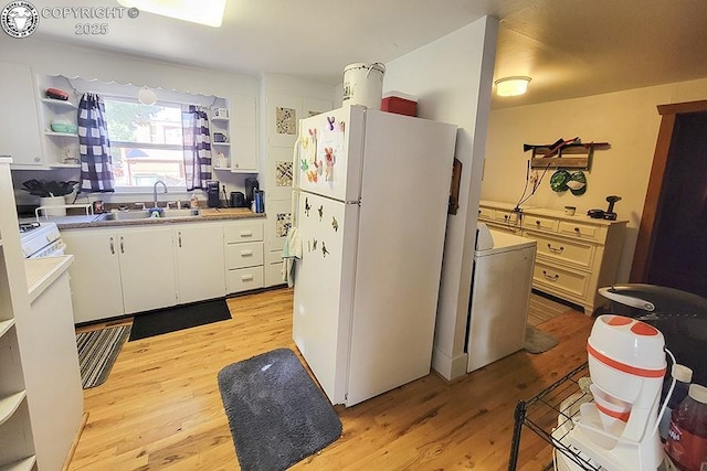 kitchen with washer / dryer, sink, white cabinetry, light hardwood / wood-style flooring, and white fridge