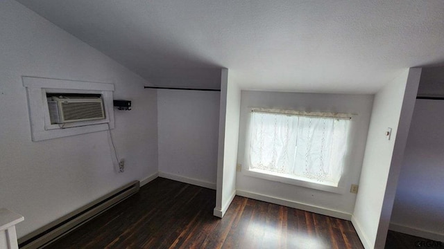 unfurnished bedroom with vaulted ceiling, dark hardwood / wood-style floors, a wall mounted AC, baseboard heating, and a textured ceiling