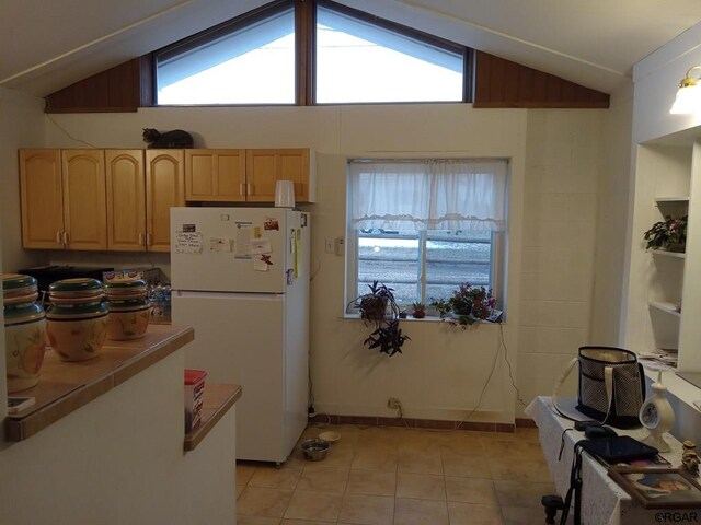 kitchen with white refrigerator, lofted ceiling, light tile patterned floors, and light brown cabinets