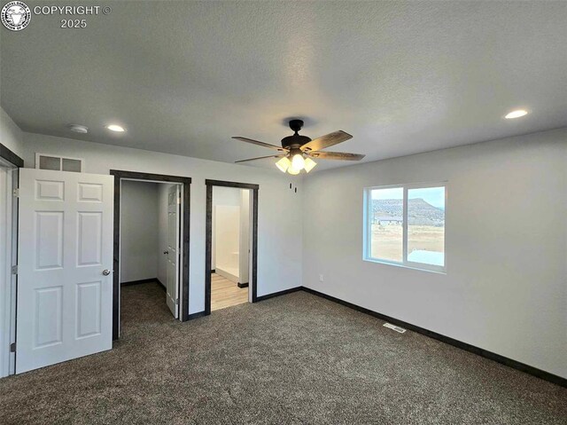 unfurnished bedroom with dark colored carpet, a walk in closet, a textured ceiling, and ceiling fan