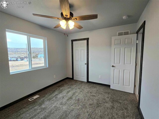 unfurnished bedroom with ceiling fan and dark colored carpet