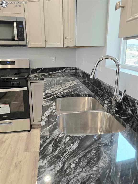 kitchen featuring sink, dark stone counters, and appliances with stainless steel finishes