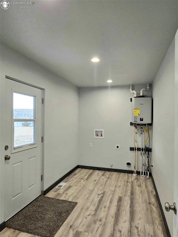 washroom featuring electric dryer hookup, washer hookup, light hardwood / wood-style flooring, and tankless water heater