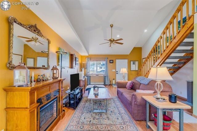 living area featuring lofted ceiling, light wood finished floors, a fireplace, and stairs