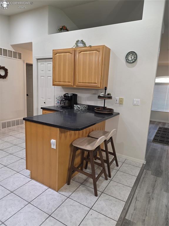 2823 River Run Ct, Canon City, CO 81212 - kitchen featuring light tile patterned floors, a kitchen bar, dark countertops, a peninsula, and high vaulted ceiling