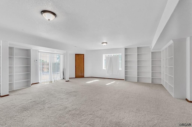 empty room featuring built in shelves, light colored carpet, and a textured ceiling