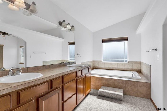 bathroom featuring vanity, vaulted ceiling, a healthy amount of sunlight, and a relaxing tiled tub