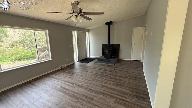 1157 County Road 119, Florence, CO 81226 - unfurnished living room featuring a textured ceiling, a wood stove, dark wood-style flooring, ceiling fan, and baseboards