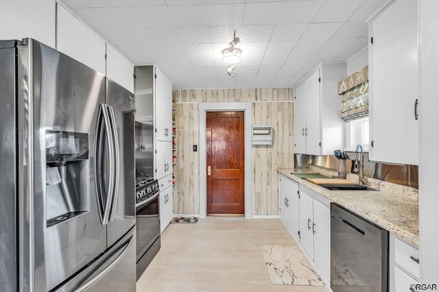 kitchen featuring wooden walls, white cabinetry, dishwasher, stainless steel fridge, and gas range