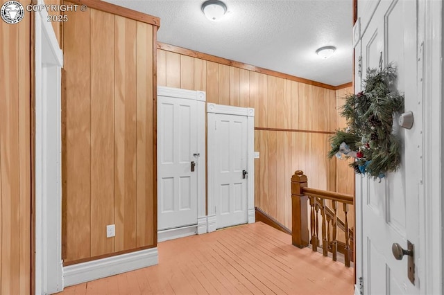 interior space with ornamental molding, wooden walls, a textured ceiling, and light hardwood / wood-style flooring