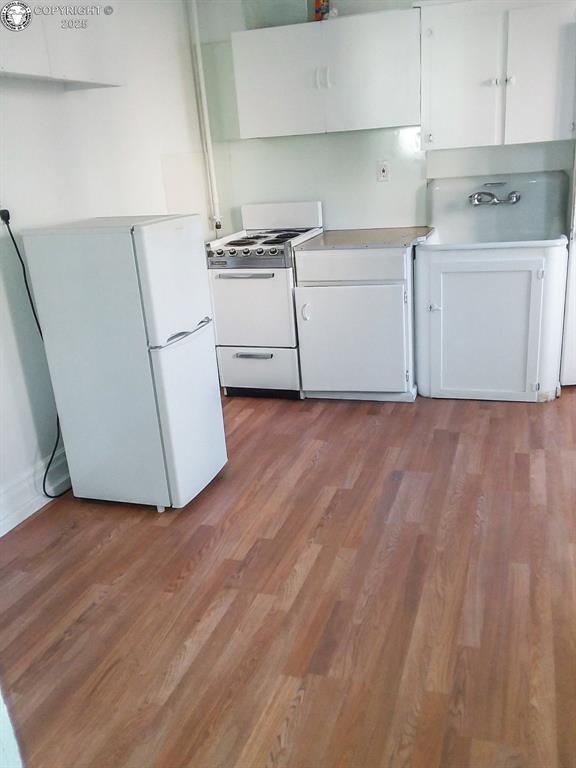 kitchen with white cabinetry, white appliances, and light hardwood / wood-style floors