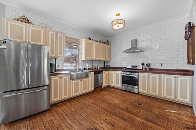 kitchen with sink, decorative backsplash, wall chimney exhaust hood, stainless steel appliances, and cream cabinetry