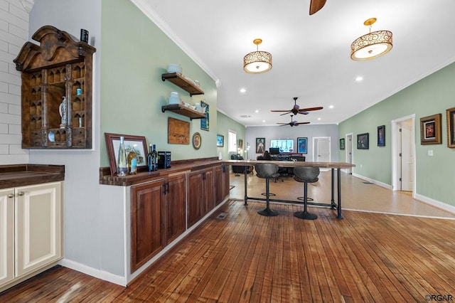 interior space featuring a kitchen bar, hardwood / wood-style flooring, ornamental molding, ceiling fan, and kitchen peninsula