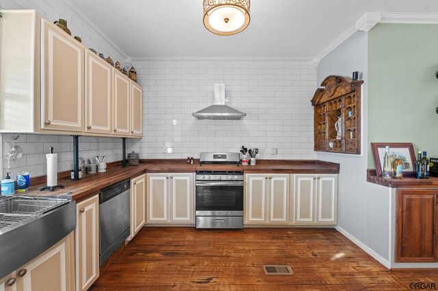 kitchen with appliances with stainless steel finishes, butcher block counters, decorative backsplash, and wall chimney range hood