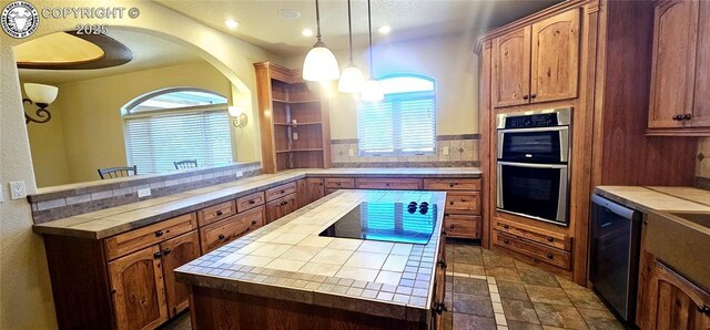 kitchen with a center island, decorative light fixtures, tile countertops, tasteful backsplash, and stainless steel double oven