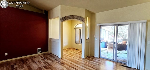 empty room featuring lofted ceiling, baseboards, arched walkways, and wood finished floors