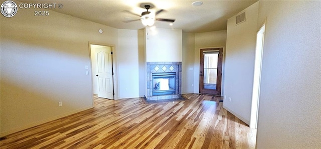 unfurnished living room featuring a tile fireplace, visible vents, baseboards, and wood finished floors