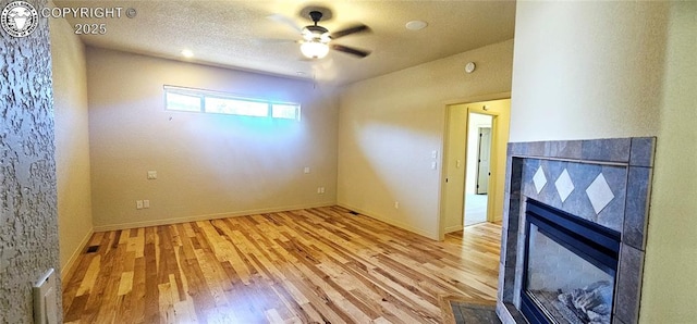 spare room featuring a textured ceiling, ceiling fan, a tile fireplace, baseboards, and light wood-type flooring