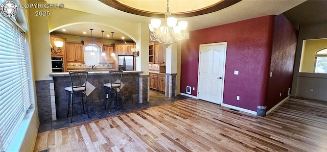 kitchen featuring arched walkways, a chandelier, a breakfast bar area, stainless steel appliances, and dark wood finished floors