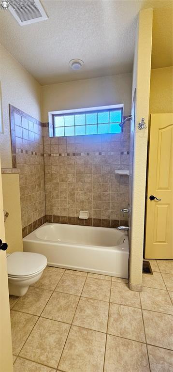 full bathroom with tile patterned flooring, visible vents, a textured ceiling, and toilet