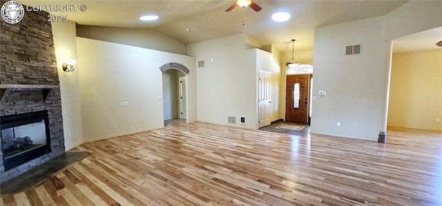 unfurnished living room with light wood finished floors, visible vents, arched walkways, a ceiling fan, and a stone fireplace