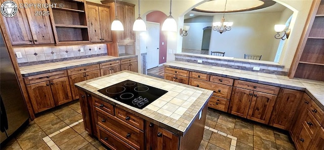 kitchen featuring black electric stovetop, tile counters, open shelves, tasteful backsplash, and decorative light fixtures