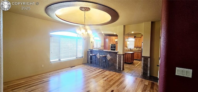 interior space featuring a notable chandelier, a peninsula, light wood finished floors, and brown cabinets