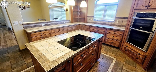 kitchen with tile countertops, hanging light fixtures, black electric stovetop, and stainless steel double oven