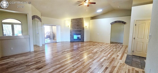 unfurnished living room with baseboards, a ceiling fan, wood finished floors, vaulted ceiling, and a stone fireplace