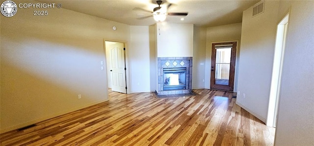 unfurnished living room with light wood-type flooring, ceiling fan, visible vents, and a tile fireplace