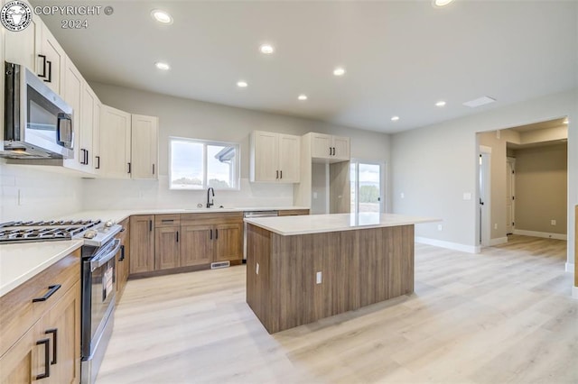 kitchen with a kitchen island, sink, white cabinets, stainless steel appliances, and light hardwood / wood-style flooring