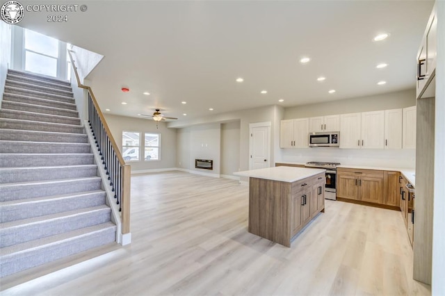 kitchen featuring ceiling fan, appliances with stainless steel finishes, white cabinetry, a kitchen island, and light wood-type flooring