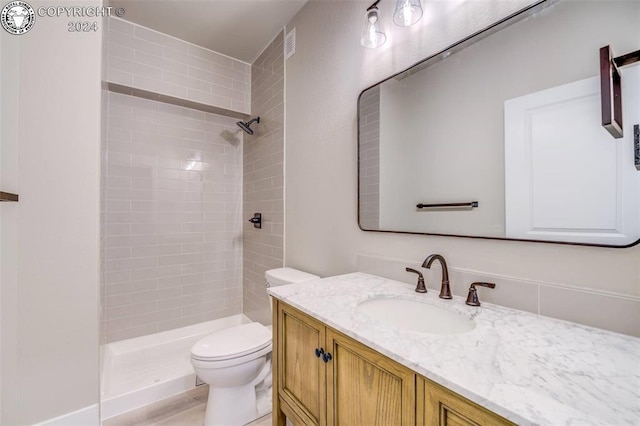 bathroom with a tile shower, vanity, and toilet