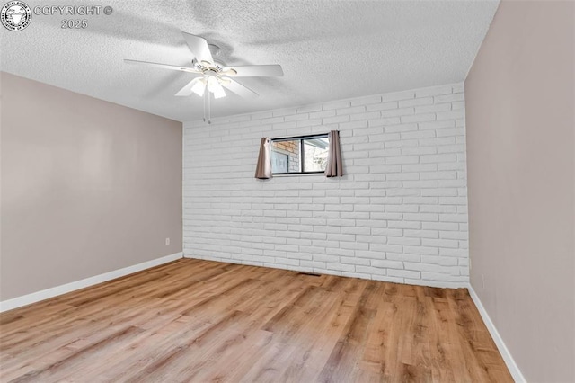 spare room featuring ceiling fan, brick wall, a textured ceiling, and light wood-type flooring