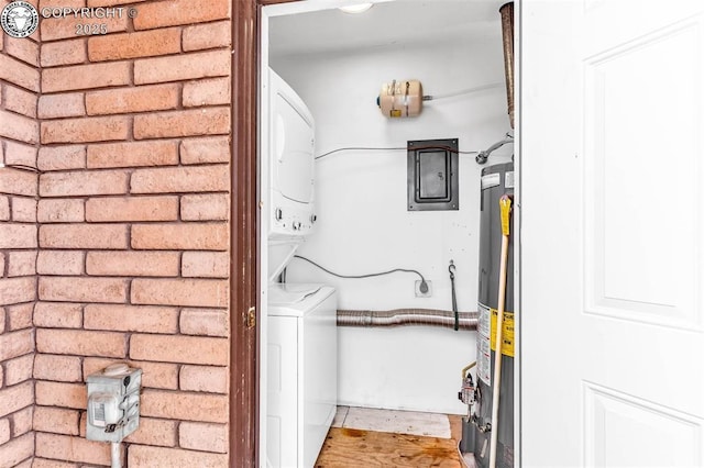 clothes washing area with stacked washing maching and dryer, water heater, and brick wall