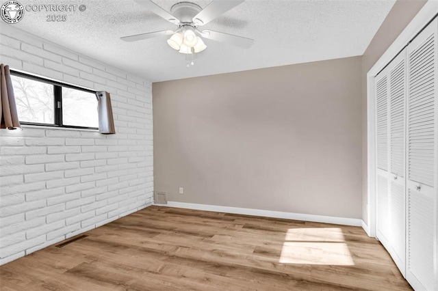 unfurnished bedroom featuring brick wall, light wood-type flooring, ceiling fan, and a closet