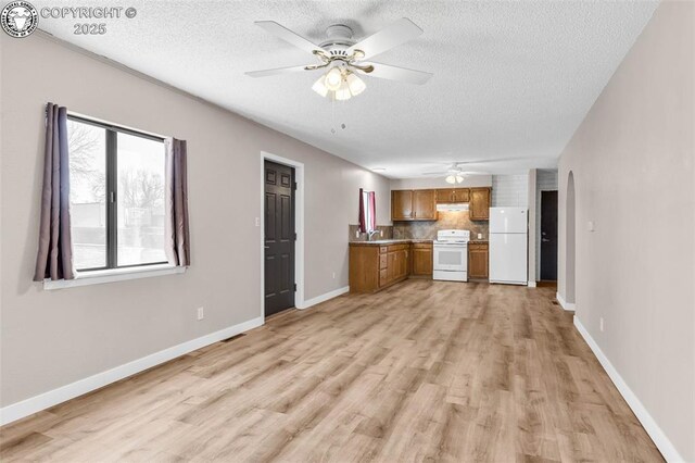 kitchen with sink, decorative backsplash, white appliances, light hardwood / wood-style floors, and a textured ceiling