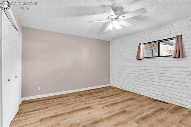 unfurnished room with brick wall, a textured ceiling, ceiling fan, and light hardwood / wood-style flooring