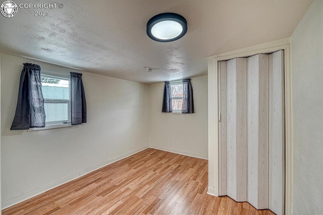 unfurnished bedroom featuring hardwood / wood-style flooring, a textured ceiling, multiple windows, and a closet