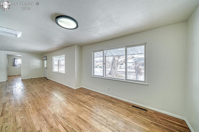 empty room with plenty of natural light, light hardwood / wood-style floors, and a textured ceiling