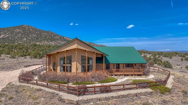 750 Roundup Rd, Westcliffe, CO 81252 - view of front facade featuring stucco siding, a porch, metal roof, fence, and a mountain view