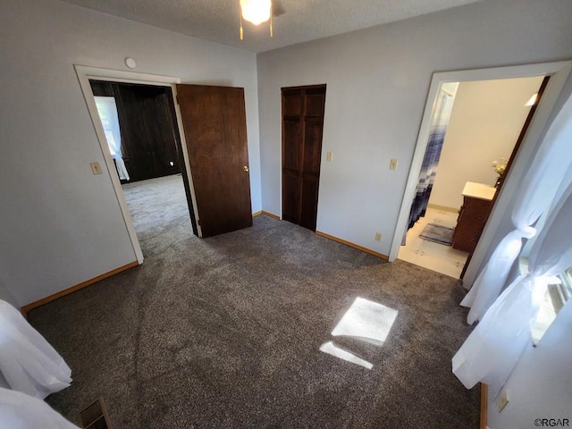 unfurnished bedroom featuring ensuite bath, dark carpet, a closet, and a textured ceiling