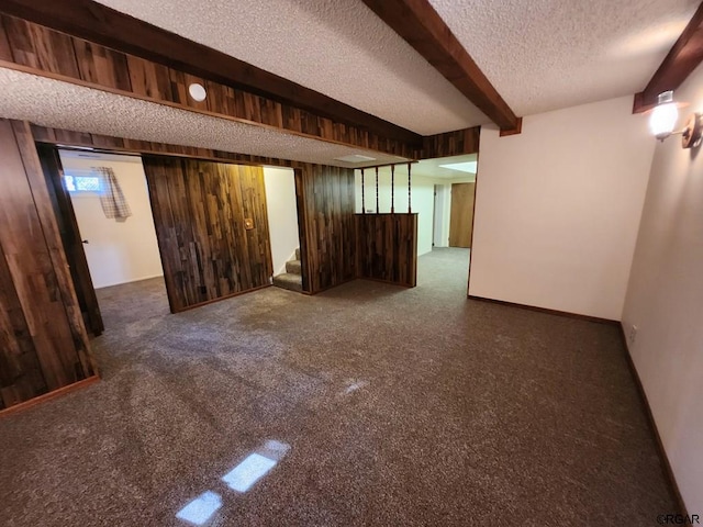 empty room featuring beam ceiling, wood walls, a textured ceiling, and dark colored carpet