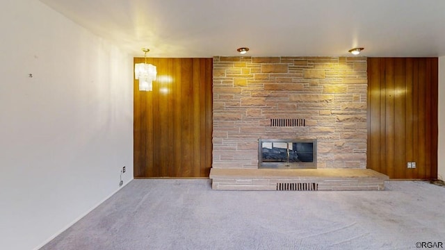 unfurnished living room with carpet flooring, wooden walls, and a stone fireplace