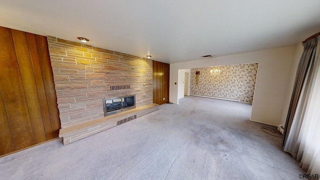 unfurnished living room featuring light colored carpet, a stone fireplace, wood walls, and a baseboard heating unit