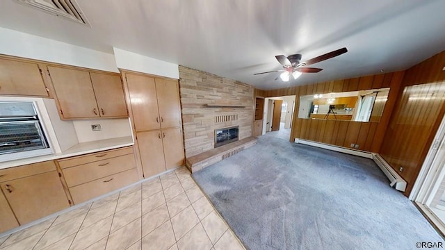 kitchen with a fireplace, wood walls, light colored carpet, baseboard heating, and ceiling fan