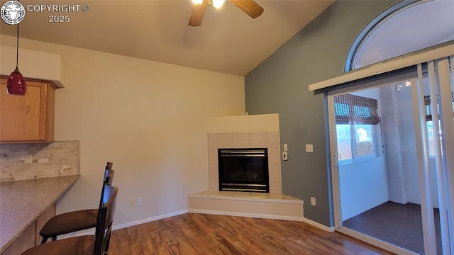 1002 Cedarcrest Dr, Pueblo, CO 81005 - unfurnished living room with wood finished floors, vaulted ceiling, a ceiling fan, and a tiled fireplace
